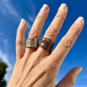 Eine Hand präsentiert zwei Ringe aus Silber. Einen breiten Silberring mit eingravierten Mustern und einen geschwärzten Wickelring aus Silberdraht mit unregelmäßig verteilten Goldtropfen.