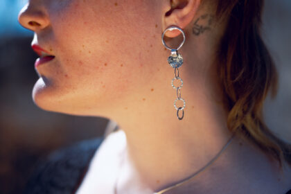 Eine Frau trägt die Kettenohhänger, dier Hintergrund ist draussen im Freien.