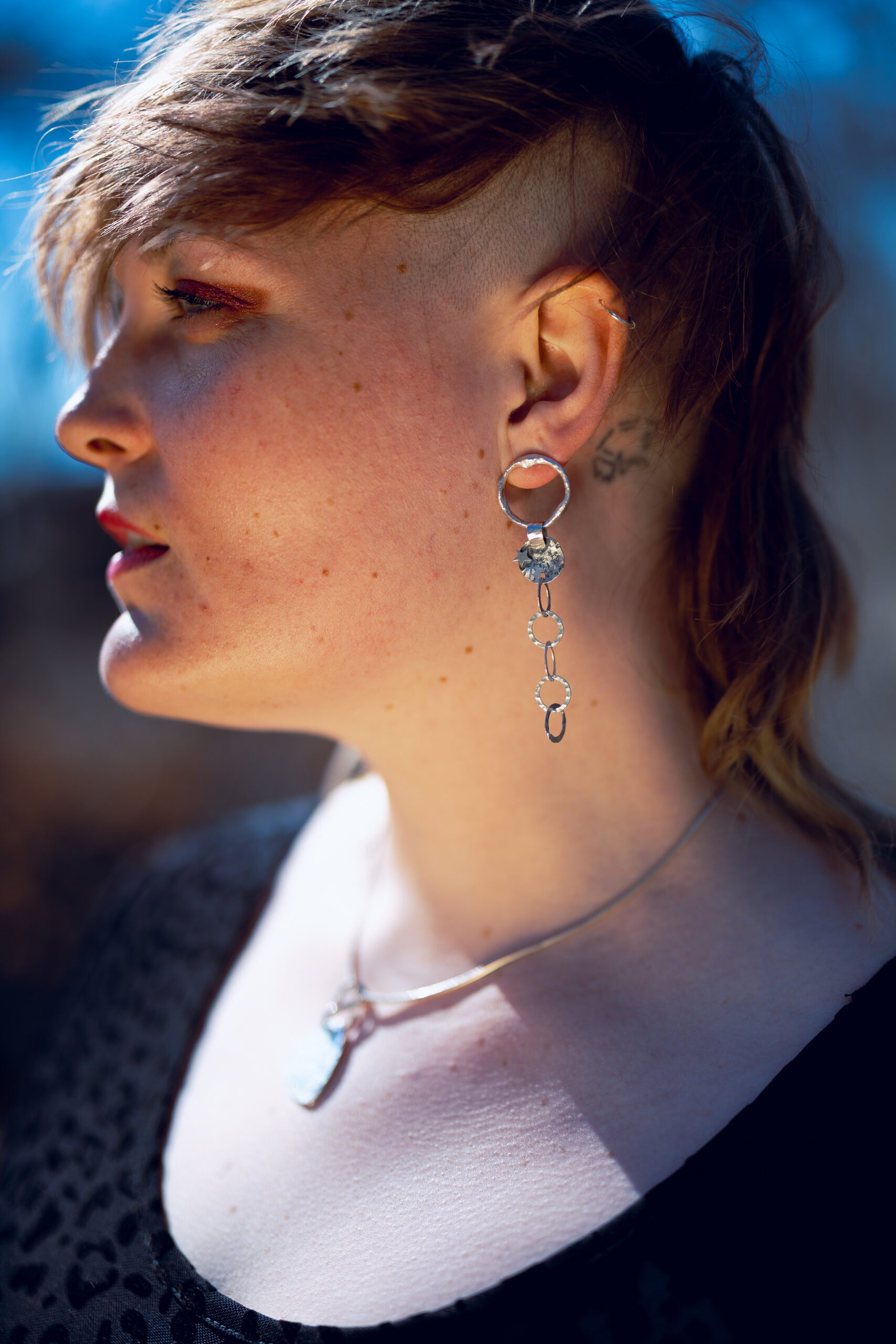 Eine Frau trägt die Kettenohhänger, dier Hintergrund ist draussen im Freien.