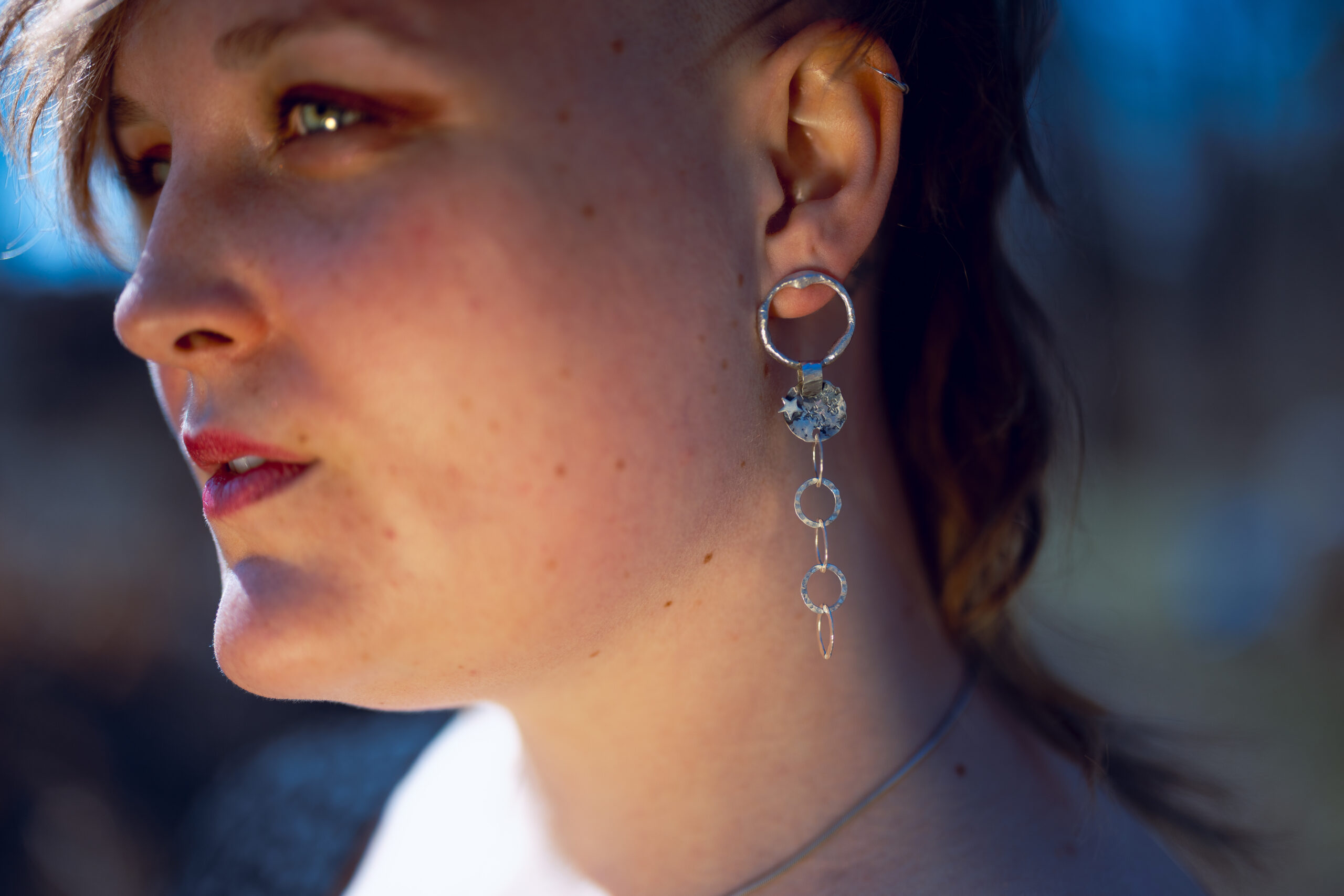 Eine Frau trägt die Kettenohhänger, dier Hintergrund ist draussen im Freien.