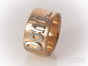 Breiter Ring in Roségold mit einem aufgesetzten Schriftzug in Silber. Text: Don't..